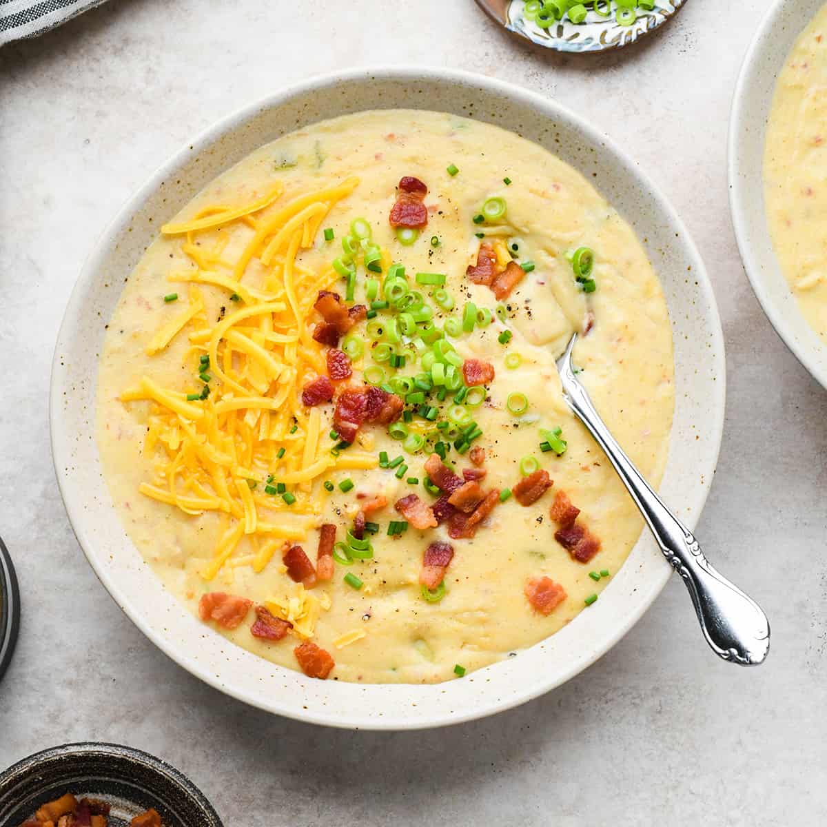 a bowl of potato soup topped with bacon, cheese, green onions and chives. 