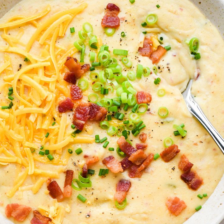 a bowl of potato soup topped with bacon, cheese, green onions and chives. 