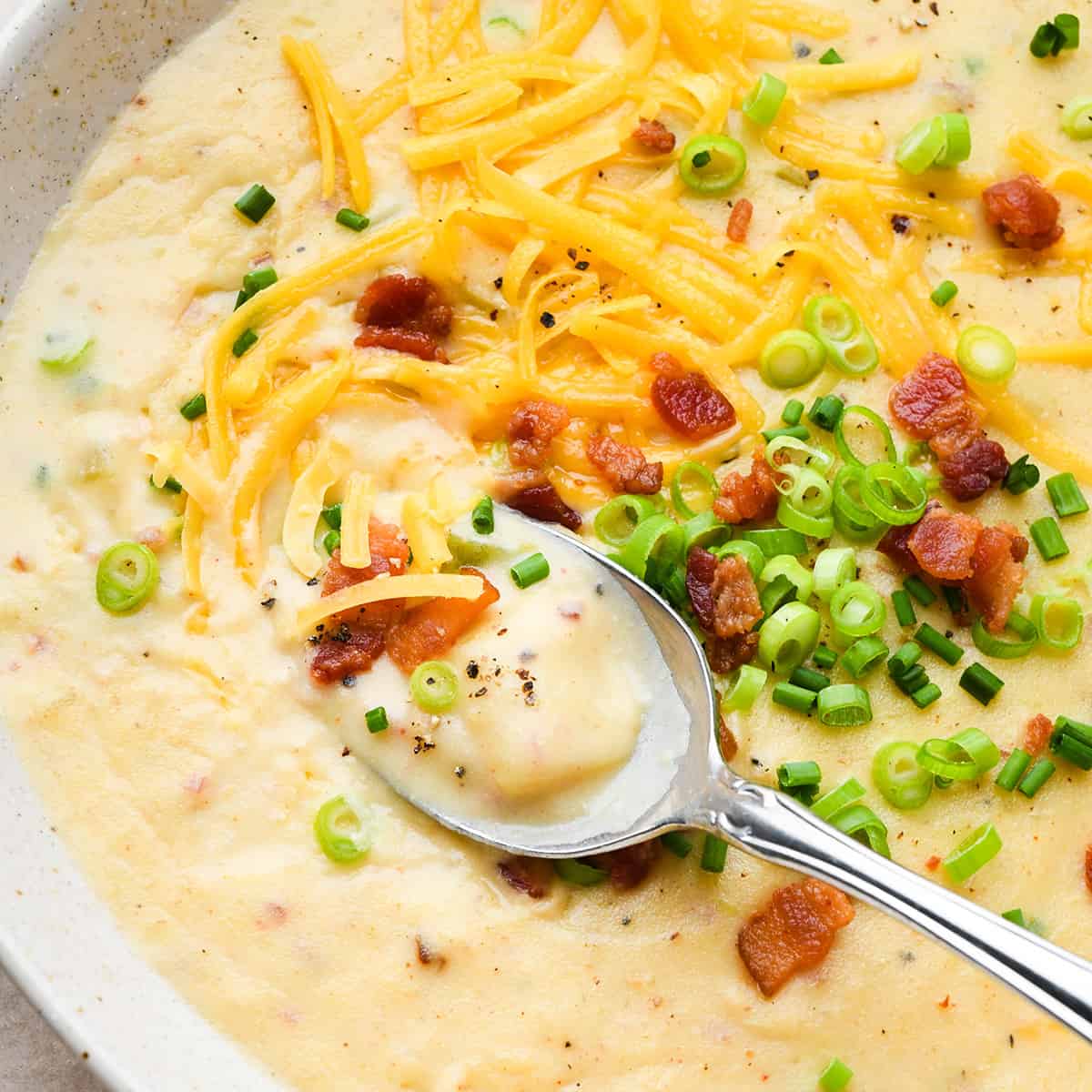 a spoon taking a scoop of Potato Soup topped with green onions, chives, bacon and cheese