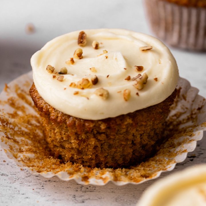 a carrot cake cupcake with the wrapper peeled down, frosted with cream cheese frosting