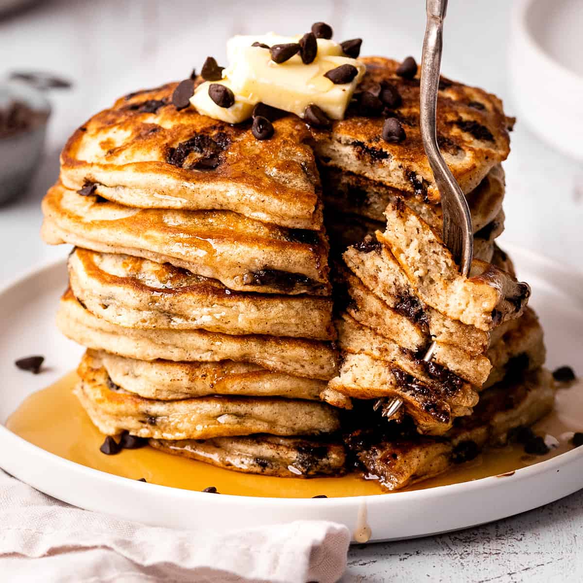 a fork taking a bite out of a stack of Chocolate Chip Pancakes with butter and syrup