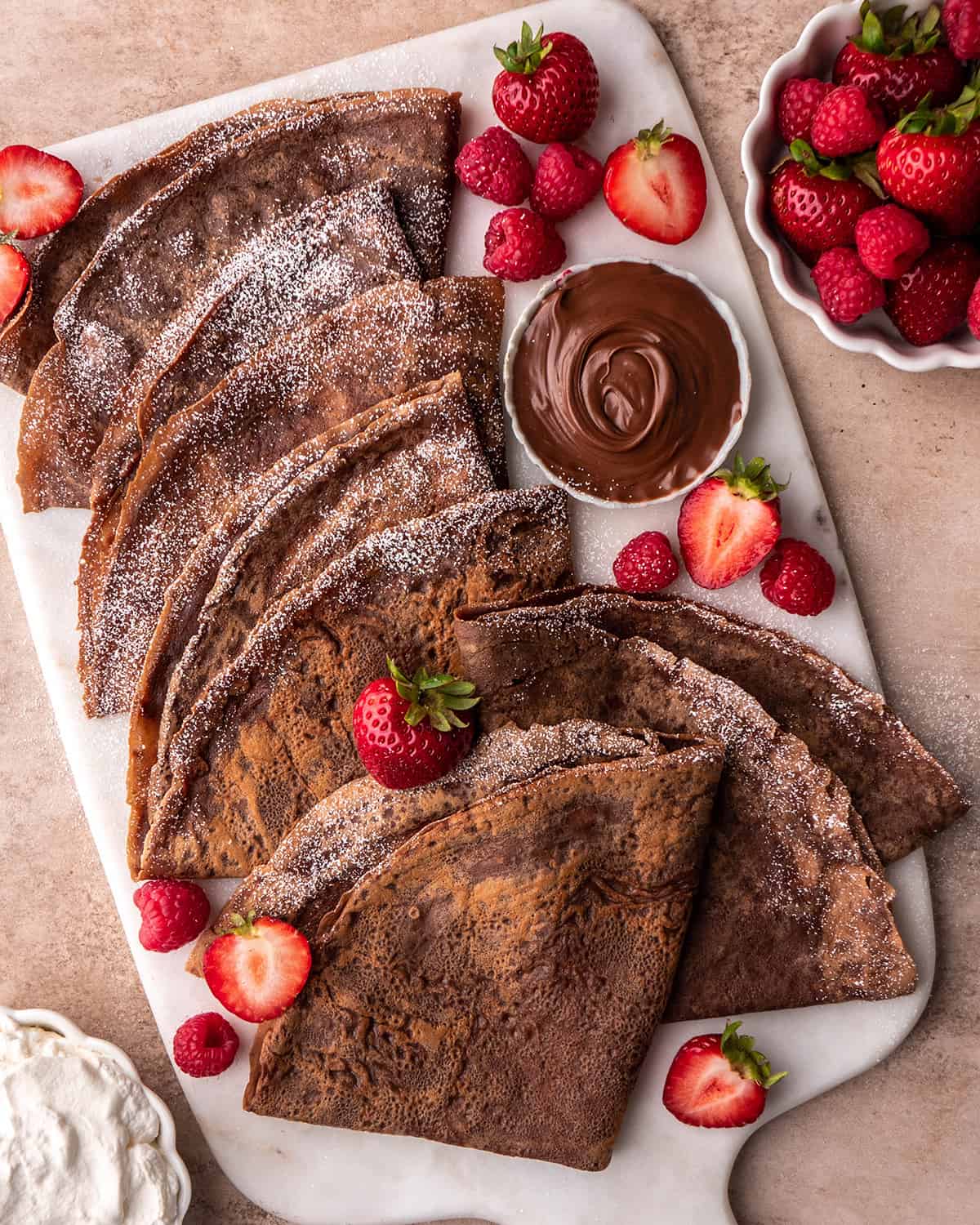 6 Chocolate Crepes folded into triangles on a plate with berries and powdered sugar on a serving platter