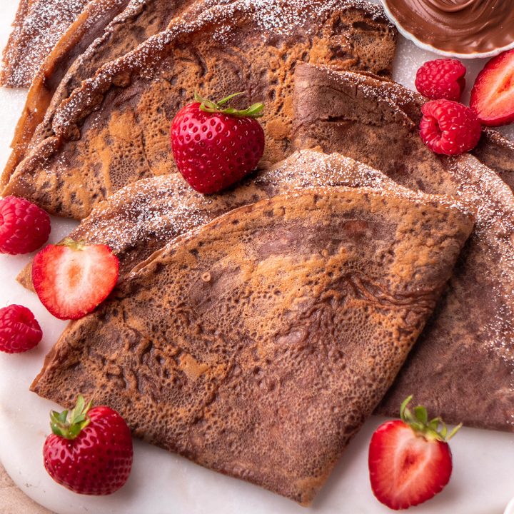 3 Chocolate Crepes folded into triangles on a plate with berries and powdered sugar
