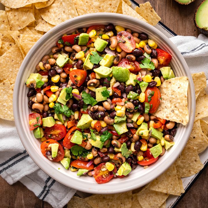 a bowl of cowboy caviar with a chip in it and surrounding it