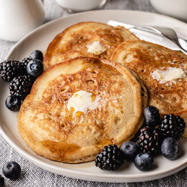 3 pancakes on a plate with butter, syrup and berries. 