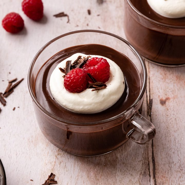 Chocolate Pudding in a glass cup with whipped cream, raspberries, and chocolate shavings