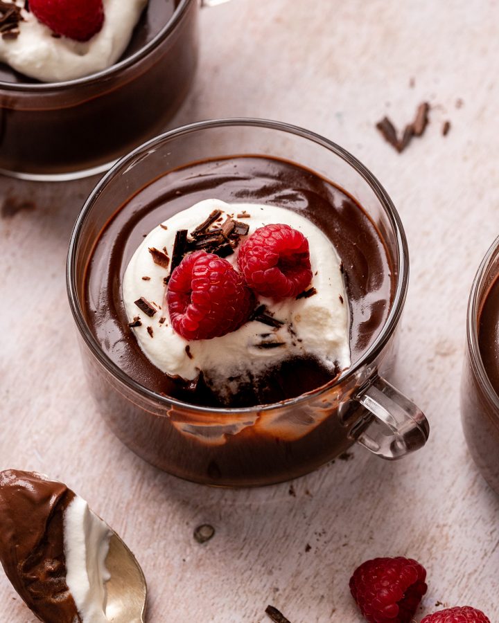 Chocolate Pudding in a glass cup with whipped cream, raspberries, and chocolate shavings