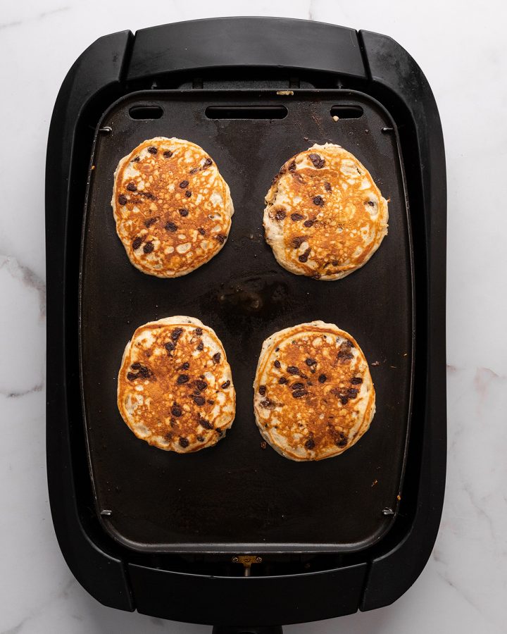 4 chocolate chip pancakes cooking on a griddle