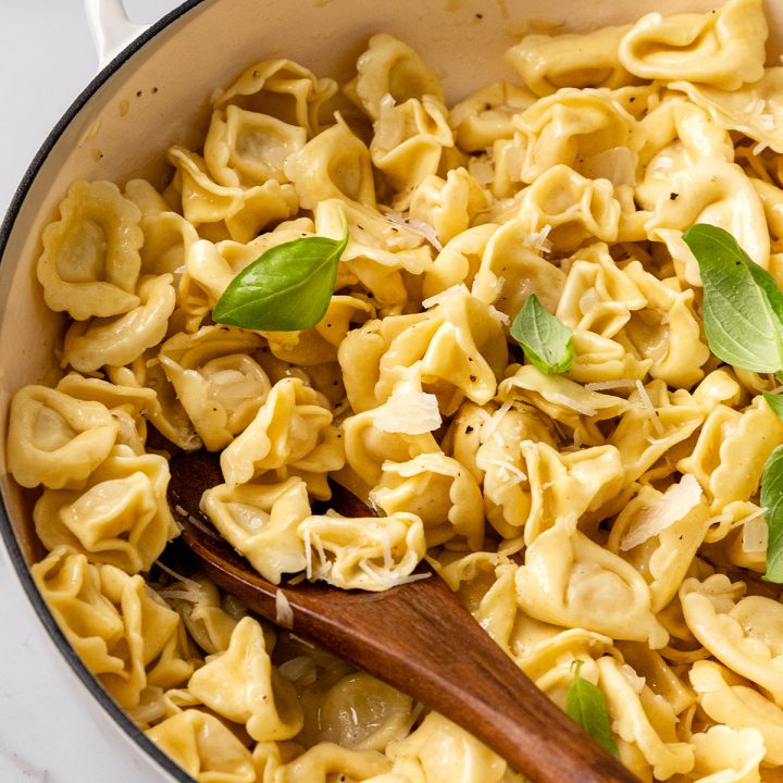 a pot of tortellini with lemon butter tortellini sauce, garnished with fresh basil and parmesan cheese
