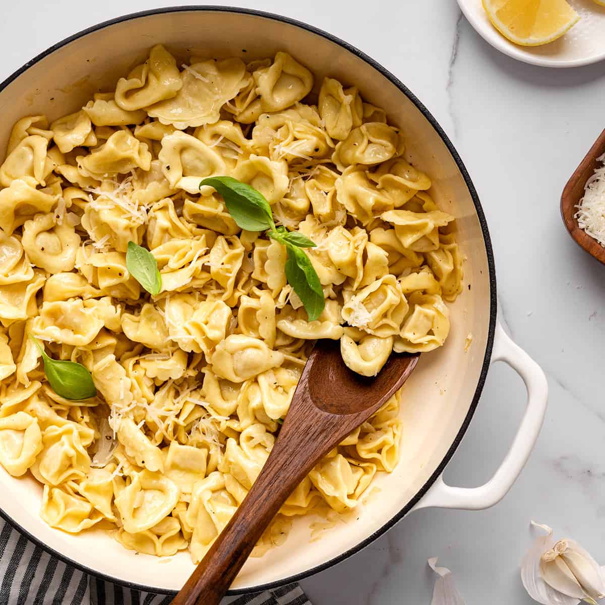 a pot of tortellini with lemon butter tortellini sauce, garnished with fresh basil and parmesan cheese