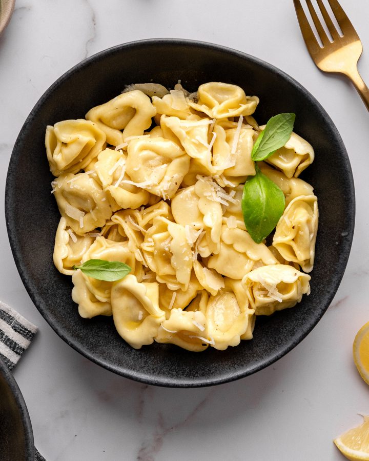 a bowl of tortellini with lemon butter tortellini sauce, garnished with fresh basil and parmesan cheese