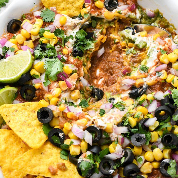 a spoon scooping Mexican 7 Layer Dip out of a pie dish