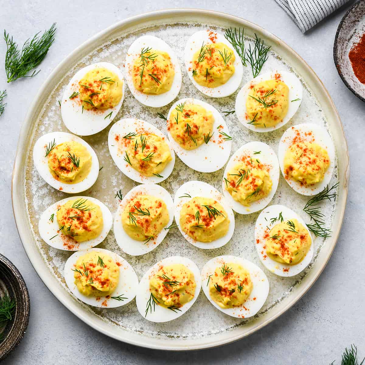 Overhead photo of a plate with 16 deviled eggs garnished with paprika and dill.