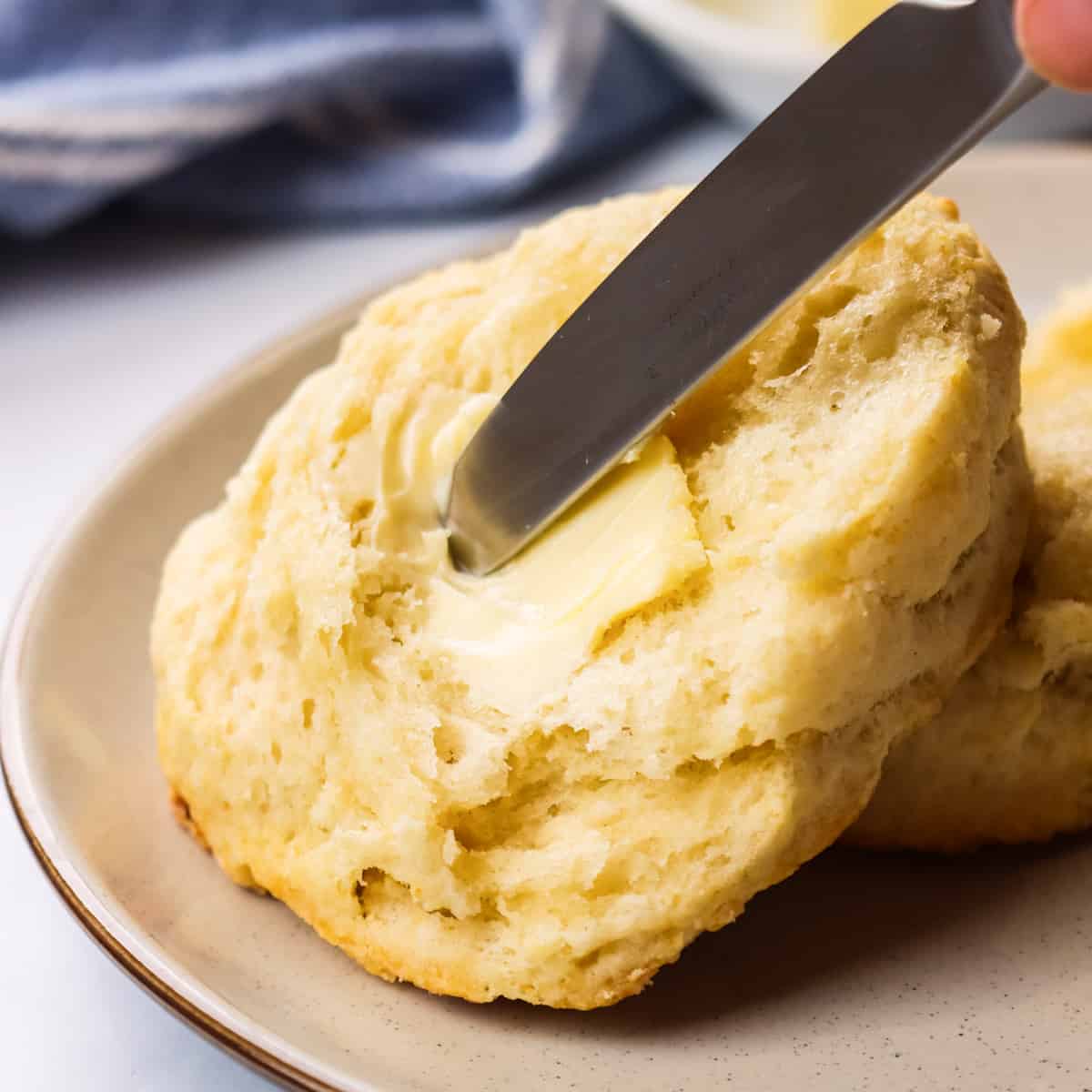 butter being spread on one half of a homemade biscuit