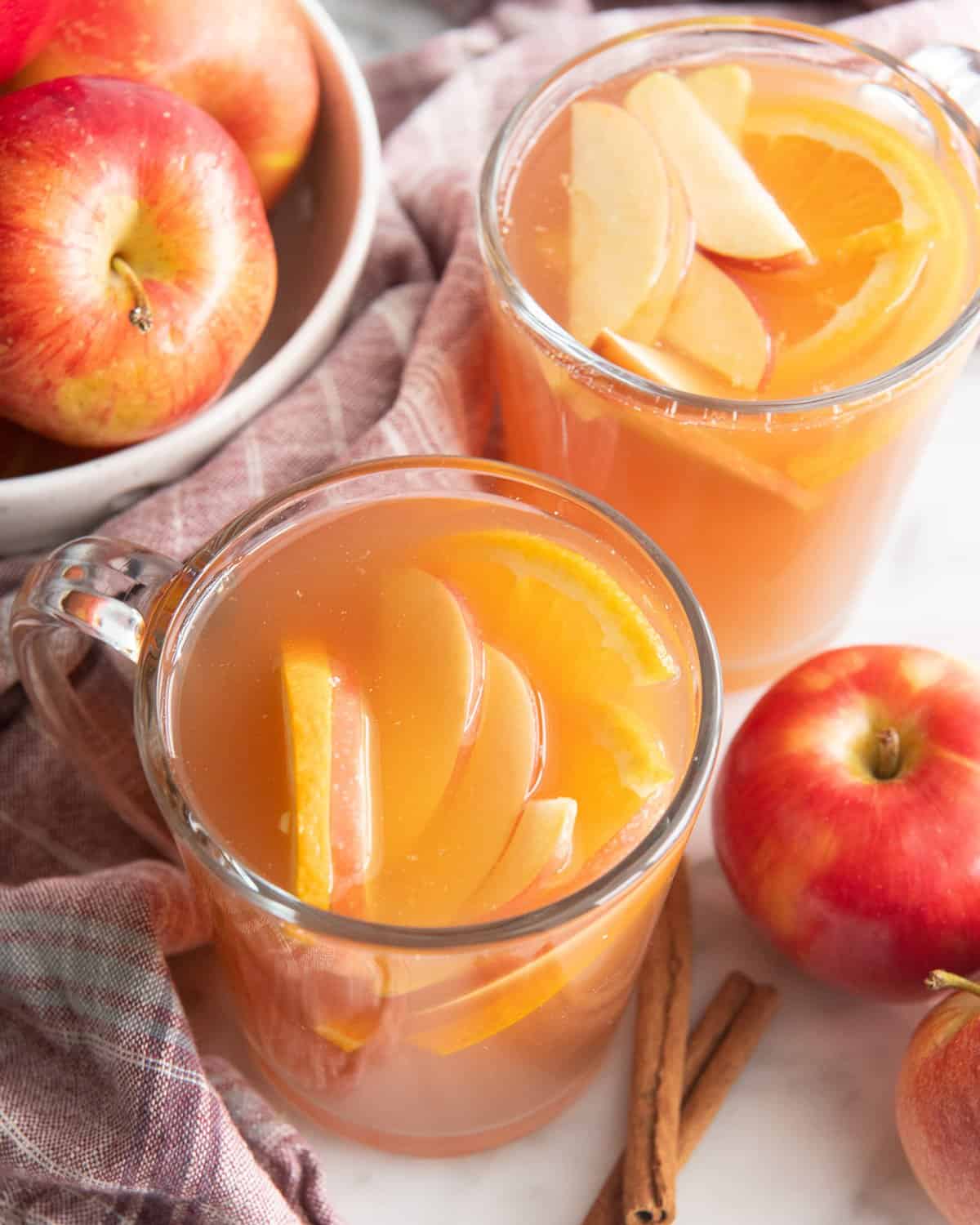 two glass mugs filled with Apple Cider and orange and apple slices