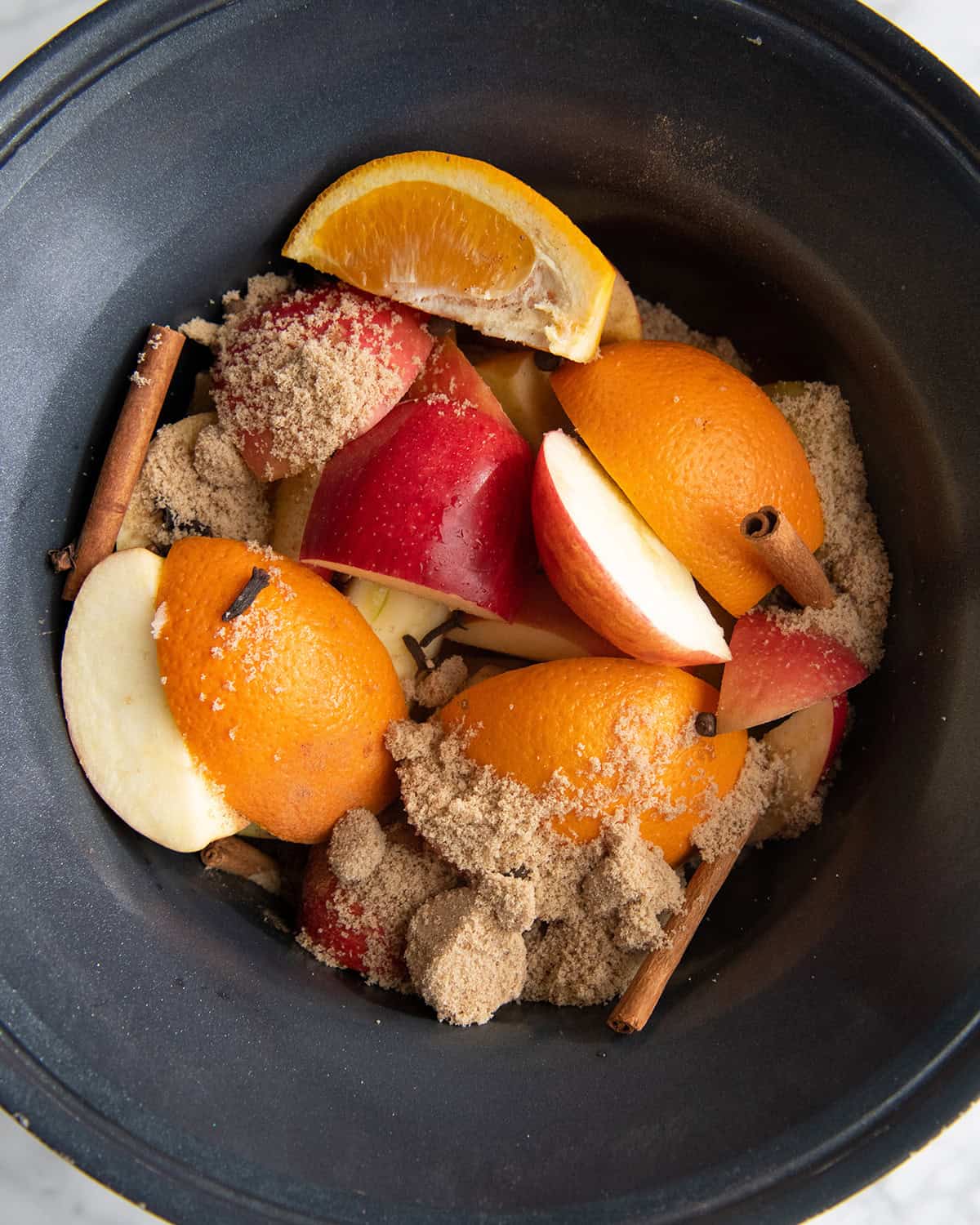 how to make apple cider recipe - ingredients apples, oranges, cinnamon sticks, brown sugar, cloves and nutmeg in a crock pot before cooking