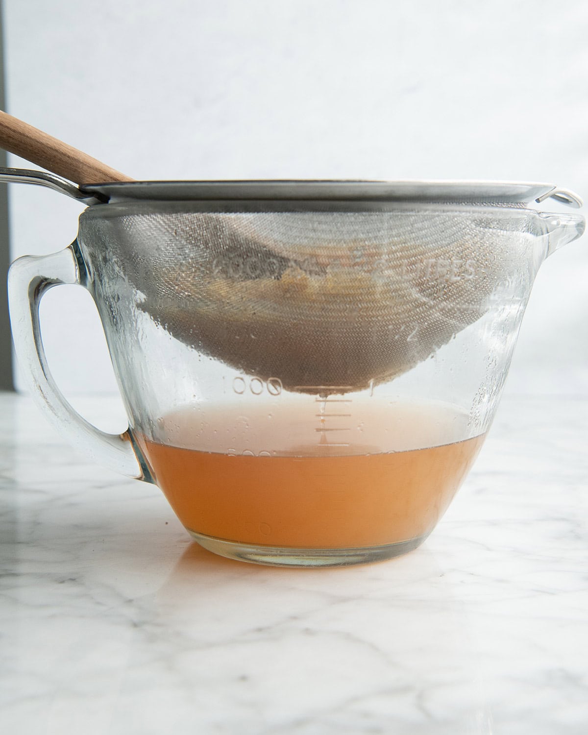how to make apple cider recipe - front photo of a mixture being strained through a fine mesh metal strainer and pressed with a wooden spoon