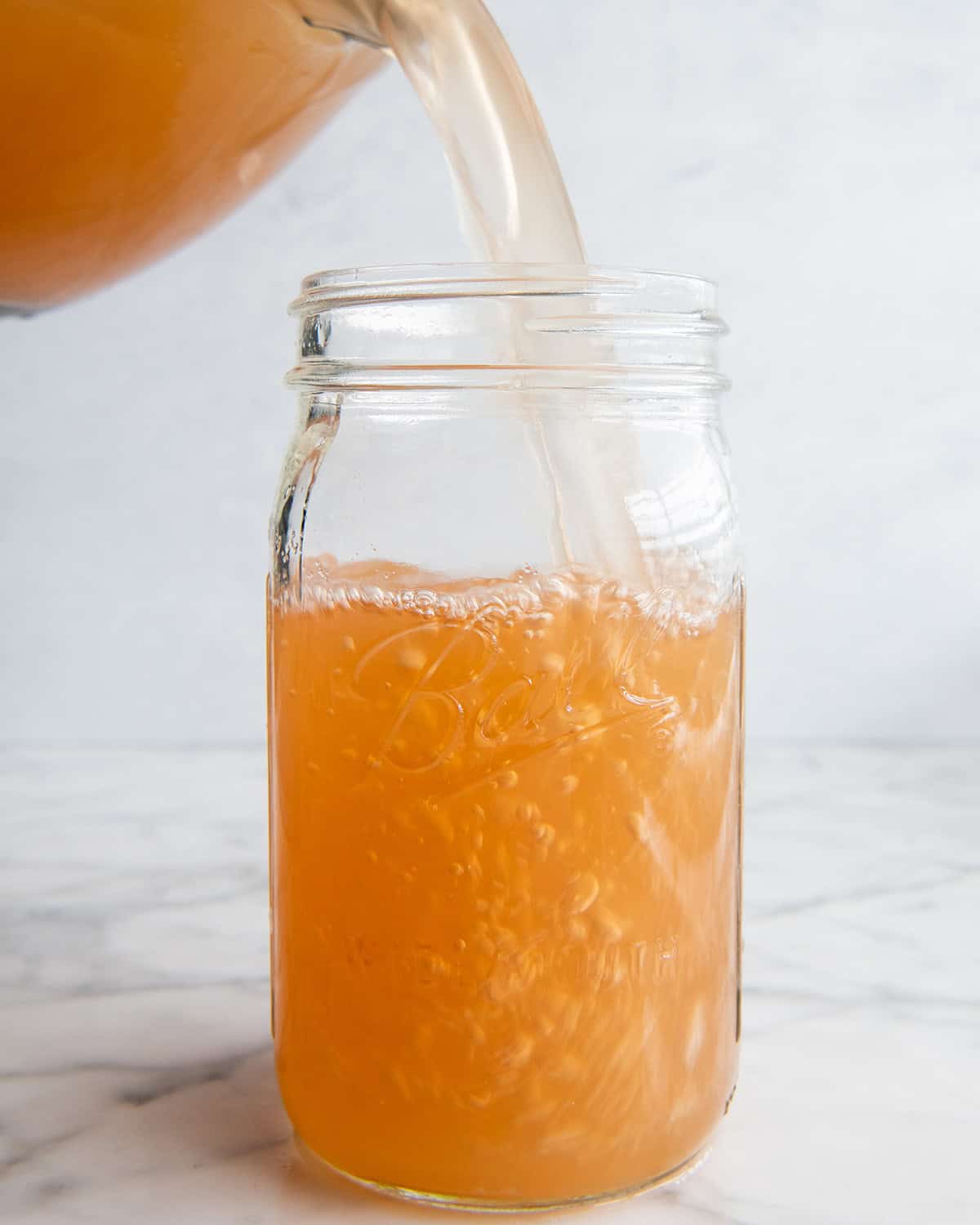 apple cider being poured from an 8 cup glass measuring cup into a large glass jar. 