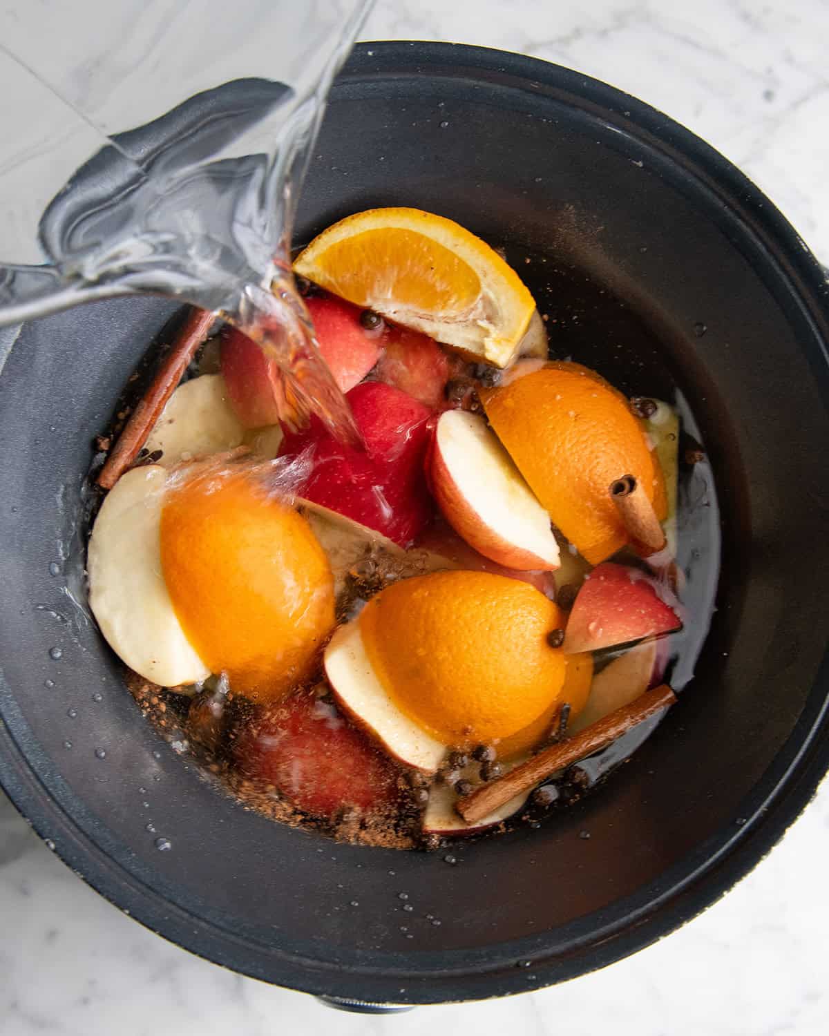 how to make apple cider recipe - water being poured over the ingredients in the crock pot