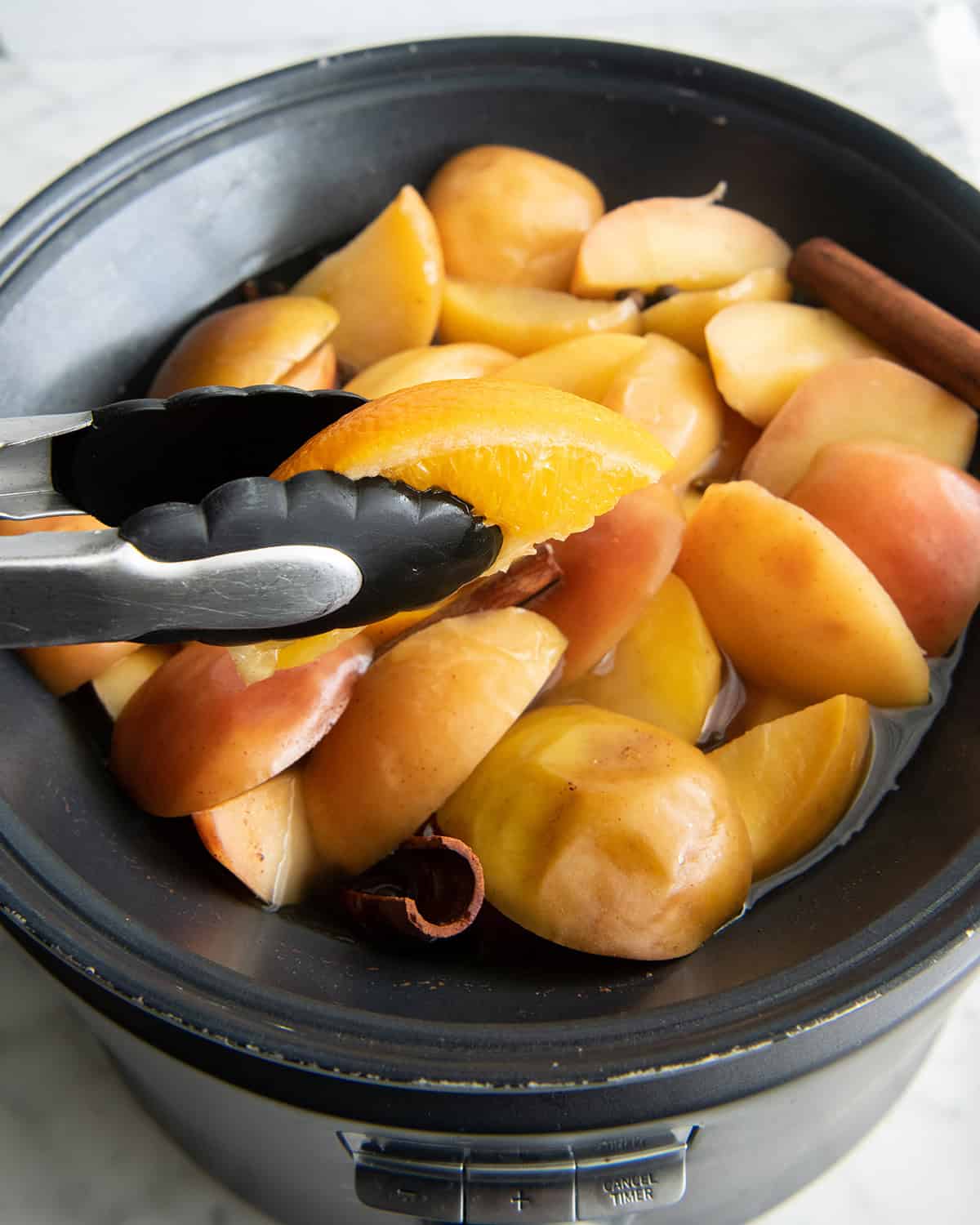 how to make apple cider recipe - tongs removing the oranges from the crock pot with the cooked apple cider ingredients