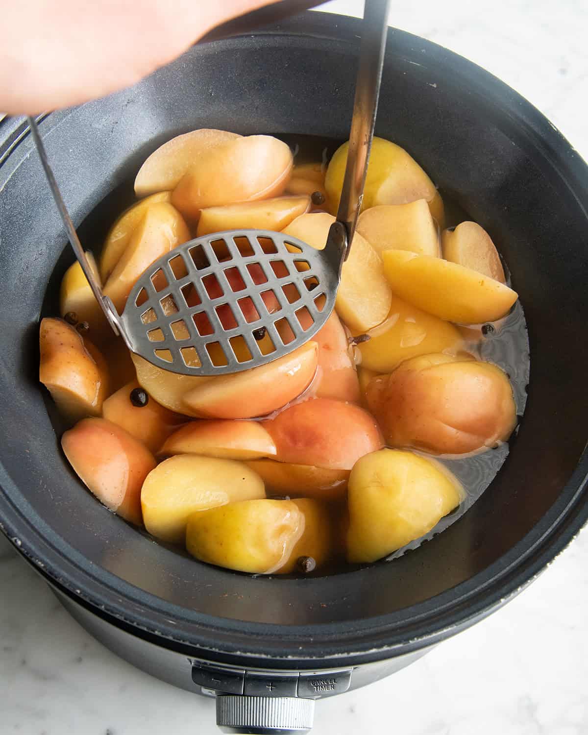 how to make apple cider recipe - a potato masher on top of the cooked cider ingredients in a crock pot