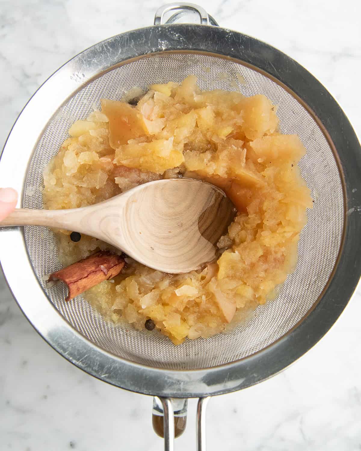 how to make apple cider recipe - overhead photo of a mixture being strained through a fine mesh metal strainer and pressed with a wooden spoon