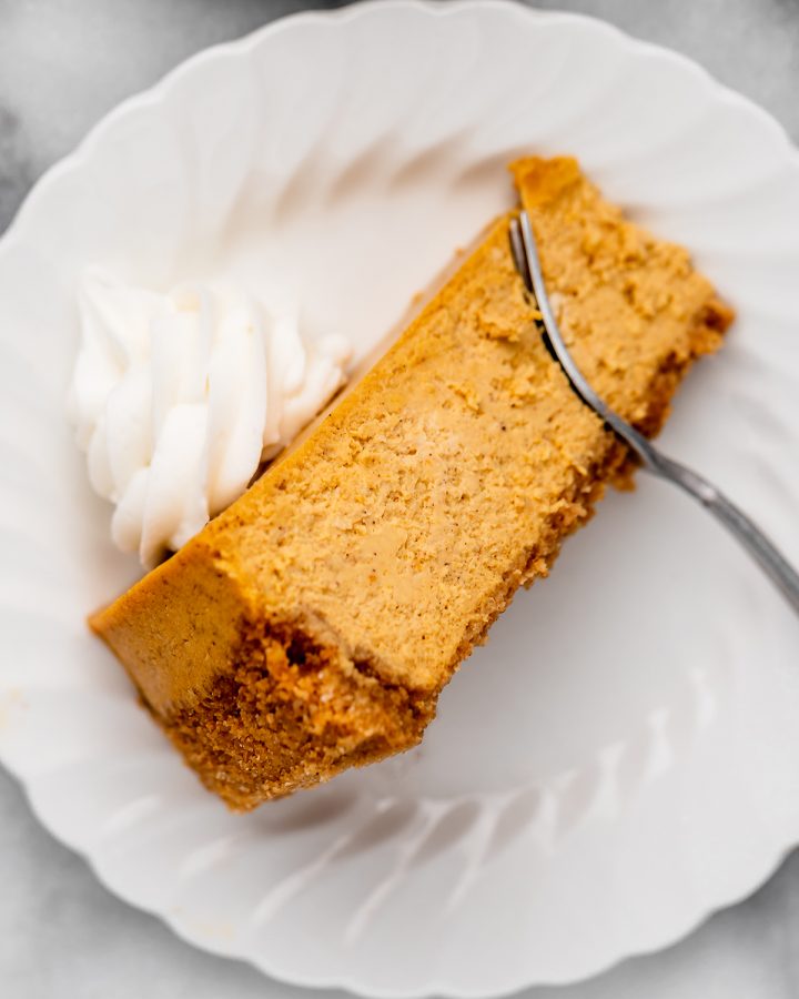 a slice of Pumpkin Cheesecake
with whipped cream on top and a fork taking a bite