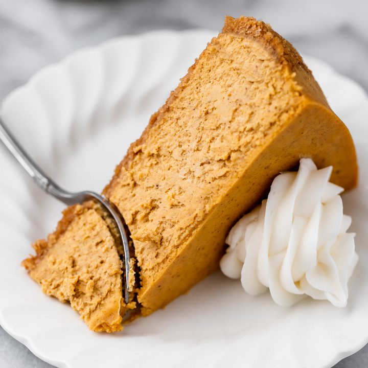 a slice of Pumpkin Cheesecake
with whipped cream on top and a fork taking a bite