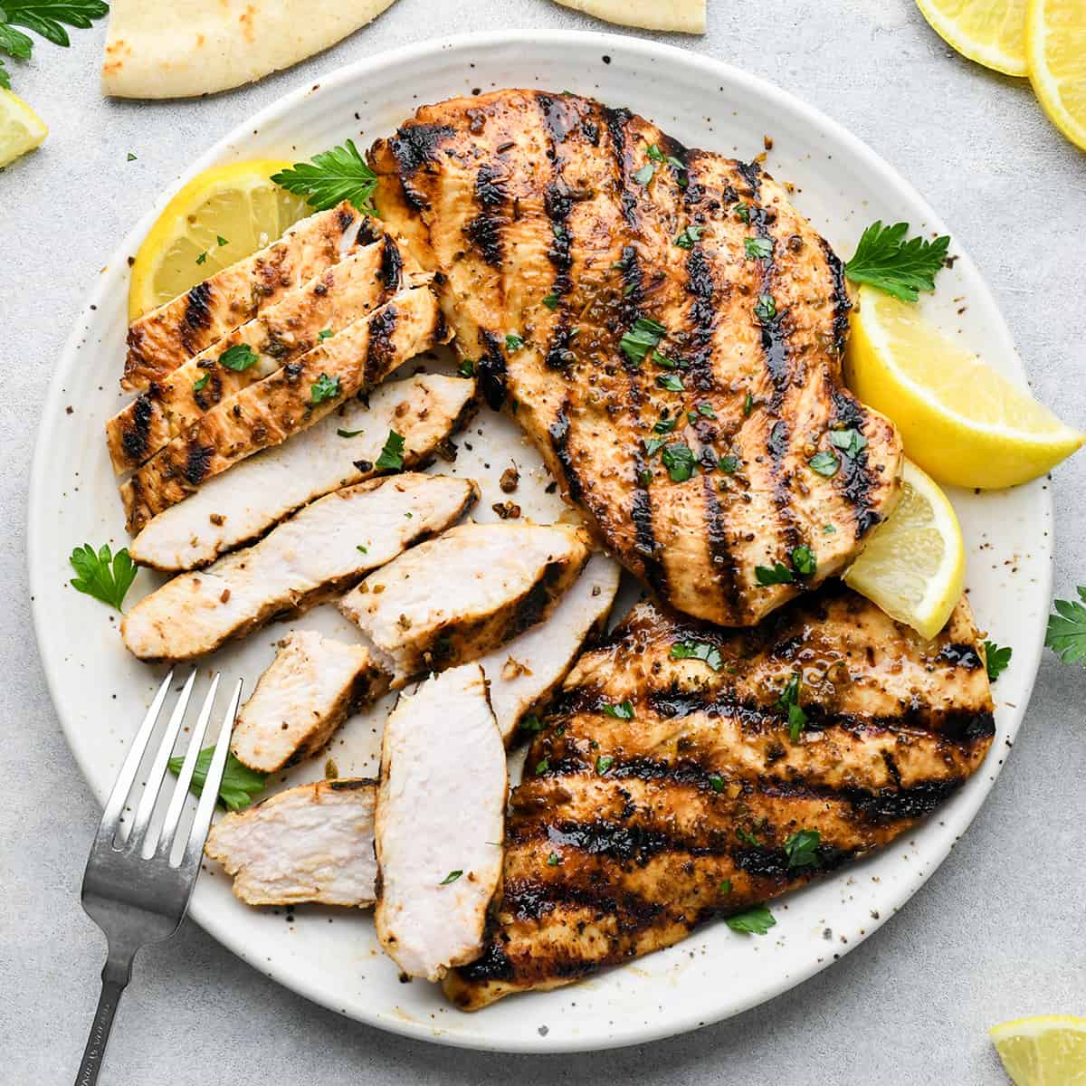 3 Greek chicken breasts on a plate, one of them cut into strips