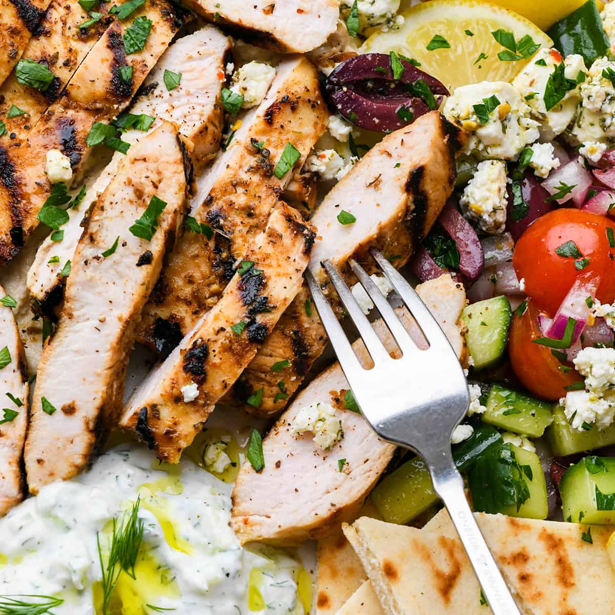 a fork taking a bite of Greek chicken on a greek salad