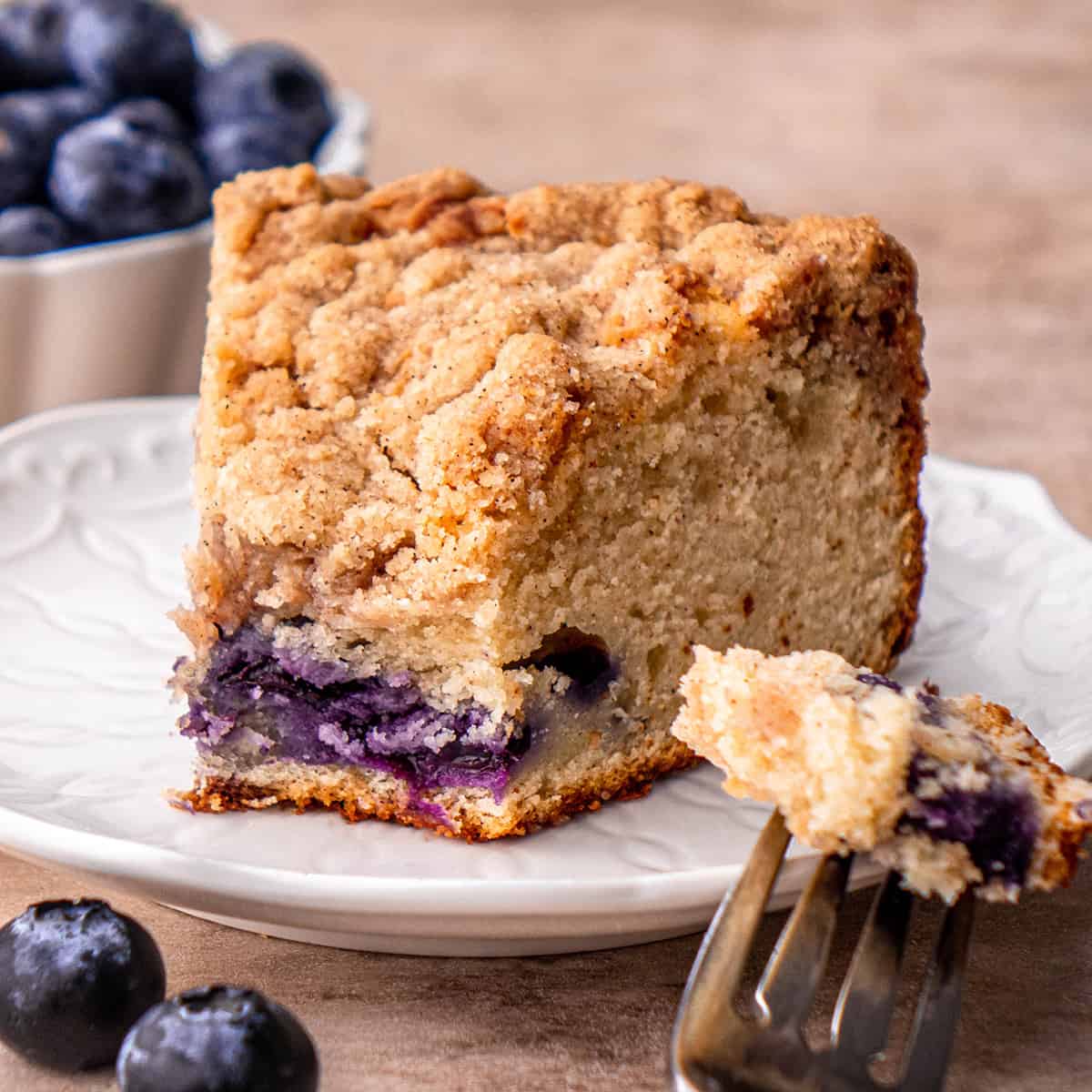 a piece of Blueberry Coffee Cake on a plate with a bite taken out of it on a fork