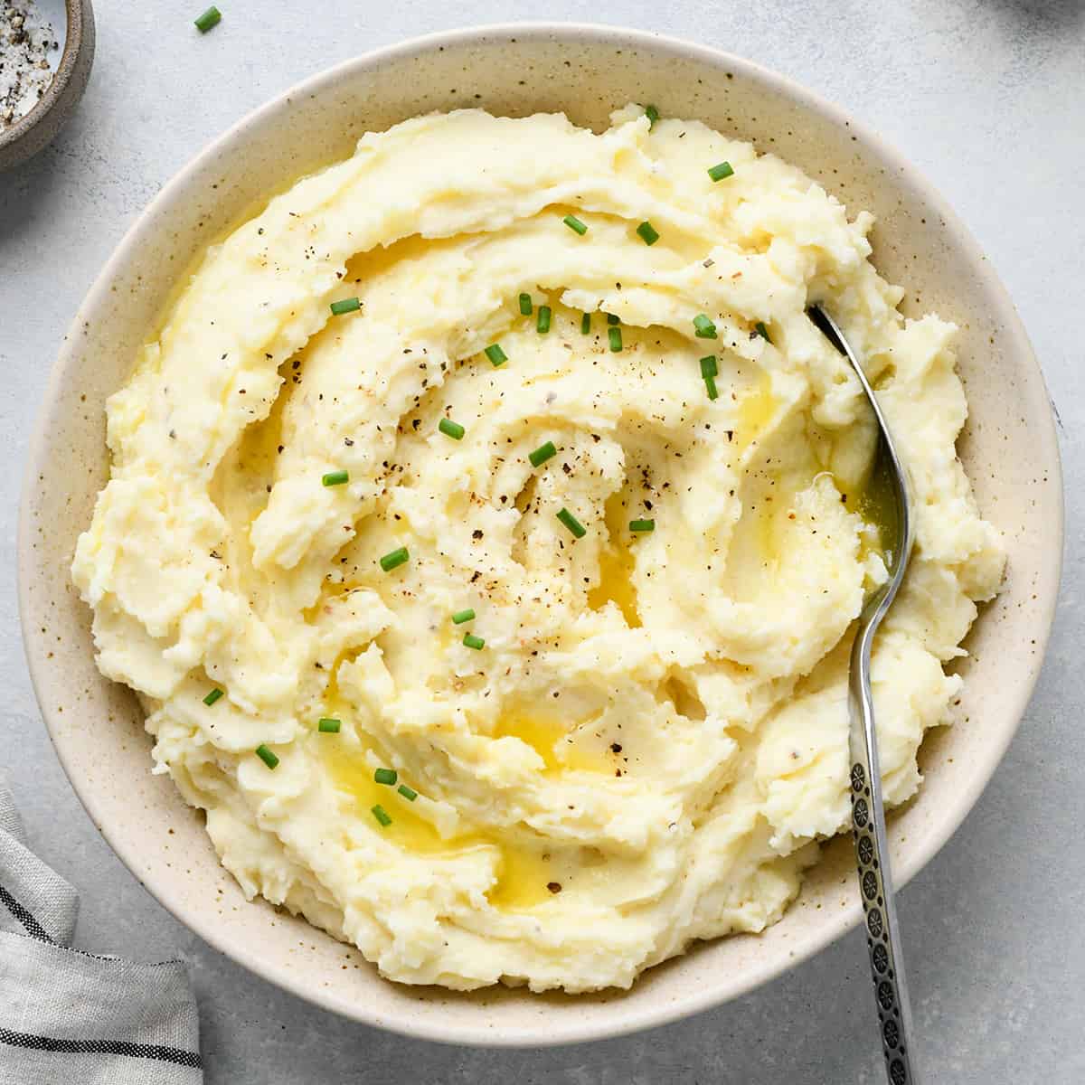 a bowl of Cream Cheese Mashed Potatoes with butter, chives, pepper and a spoon 