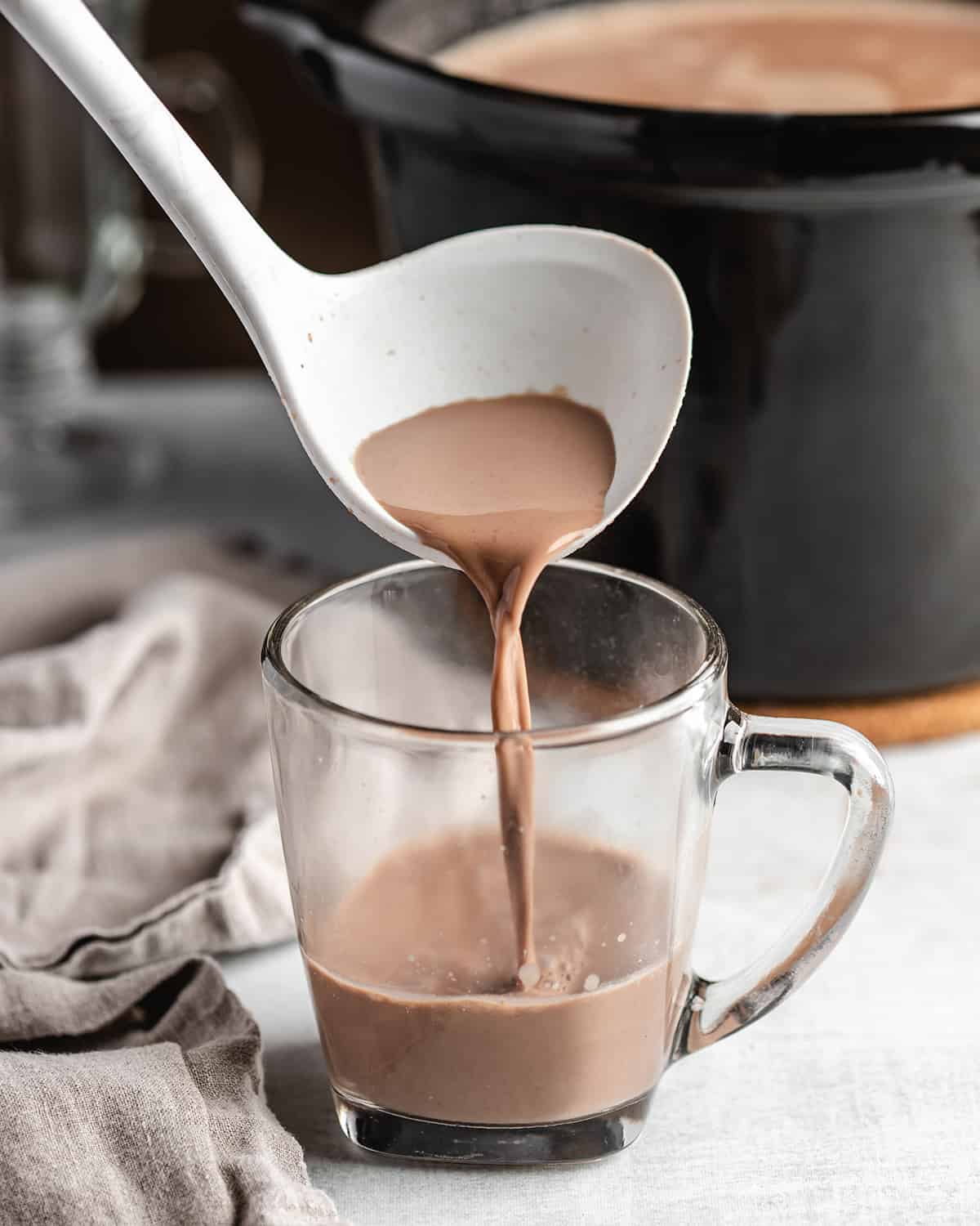 a ladle pouring Crockpot Hot Chocolate into a glass mug