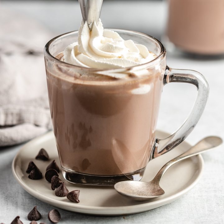 whipped cream being piped on top of a glass mug full of Crockpot Hot Chocolate
