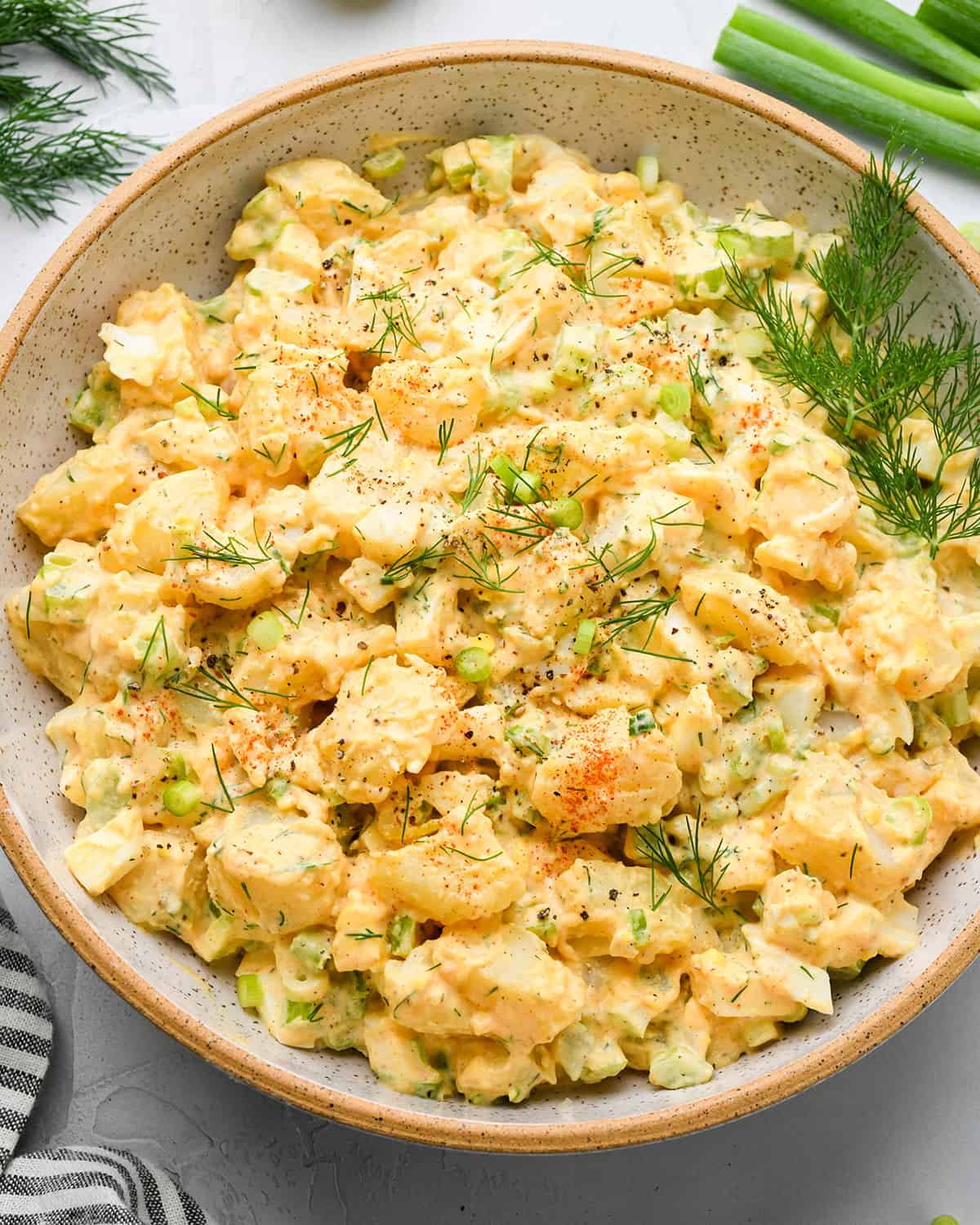 a bowl of Potato Salad garnished with dill and green onions