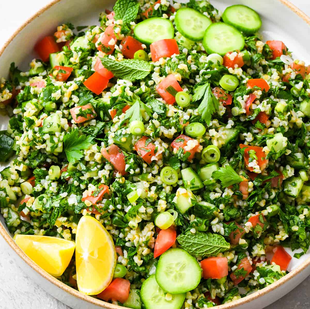 Tabbouleh in a bowl with lemons, herbs and cucumbers