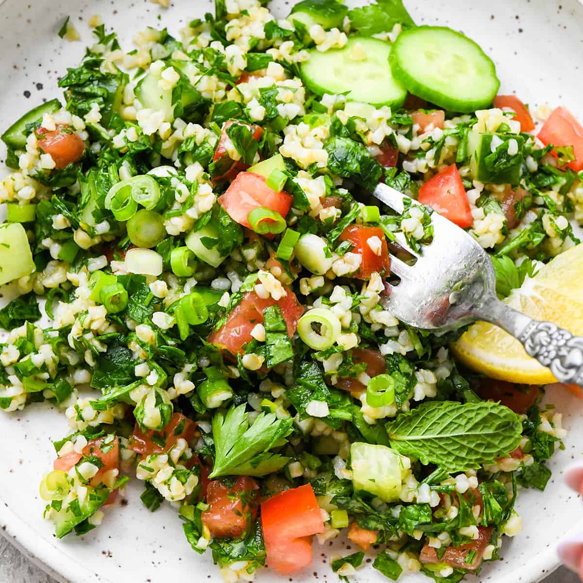 a fork taking a bite of tabbouleh on a small plate