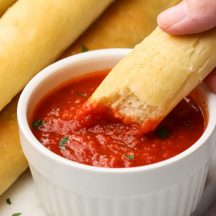 a breadstick being dipped into marinara sauce
