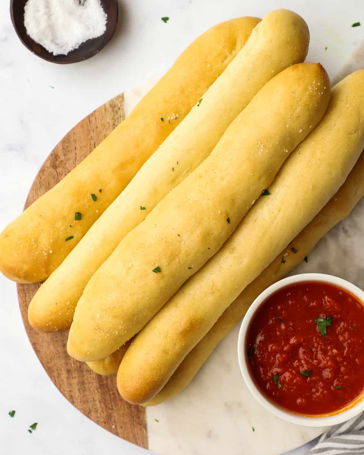 overhead view of 6 breadsticks on a serving board with marinara sauce