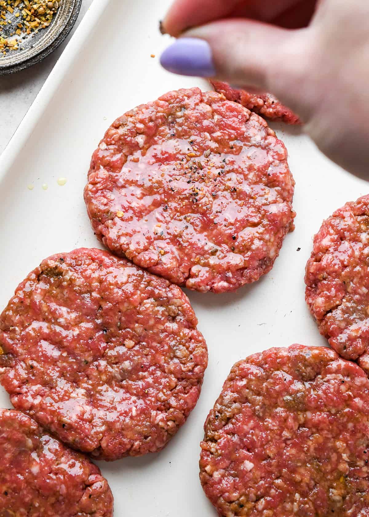 sprinkling seasoning on top of homemade hamburger patties