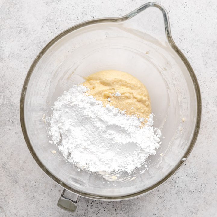 powdered sugar being added to Lemon Buttercream Frosting in a mixing bowl