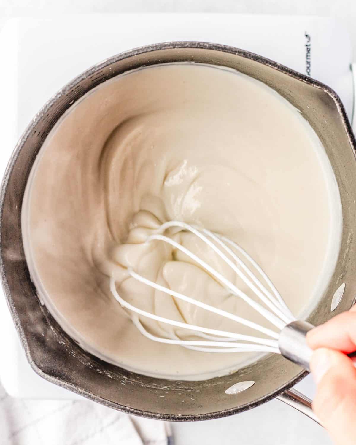 making macaroni and cheese cups sauce - thickened sauce mixture being whisked in a cast iron skillet with a white whisk