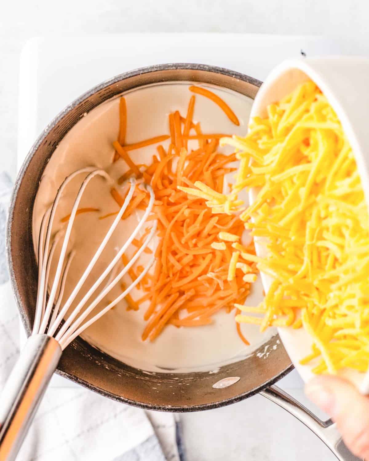 making macaroni and cheese cups sauce - cheese being added to the wet mixture in a saucepan with a whisk int eh saucepan
