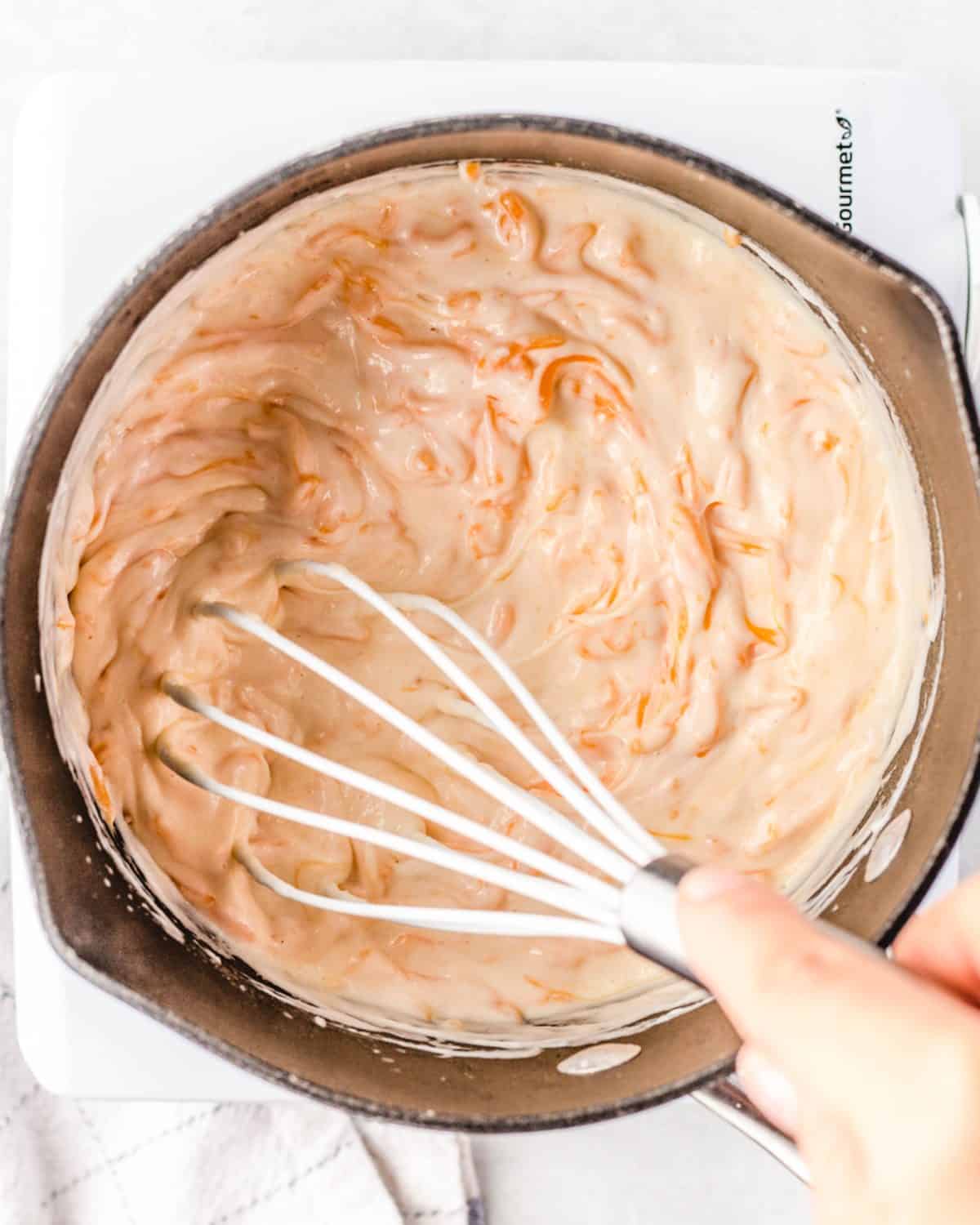 making macaroni and cheese cups sauce - the sauce being whisked with a white whisk