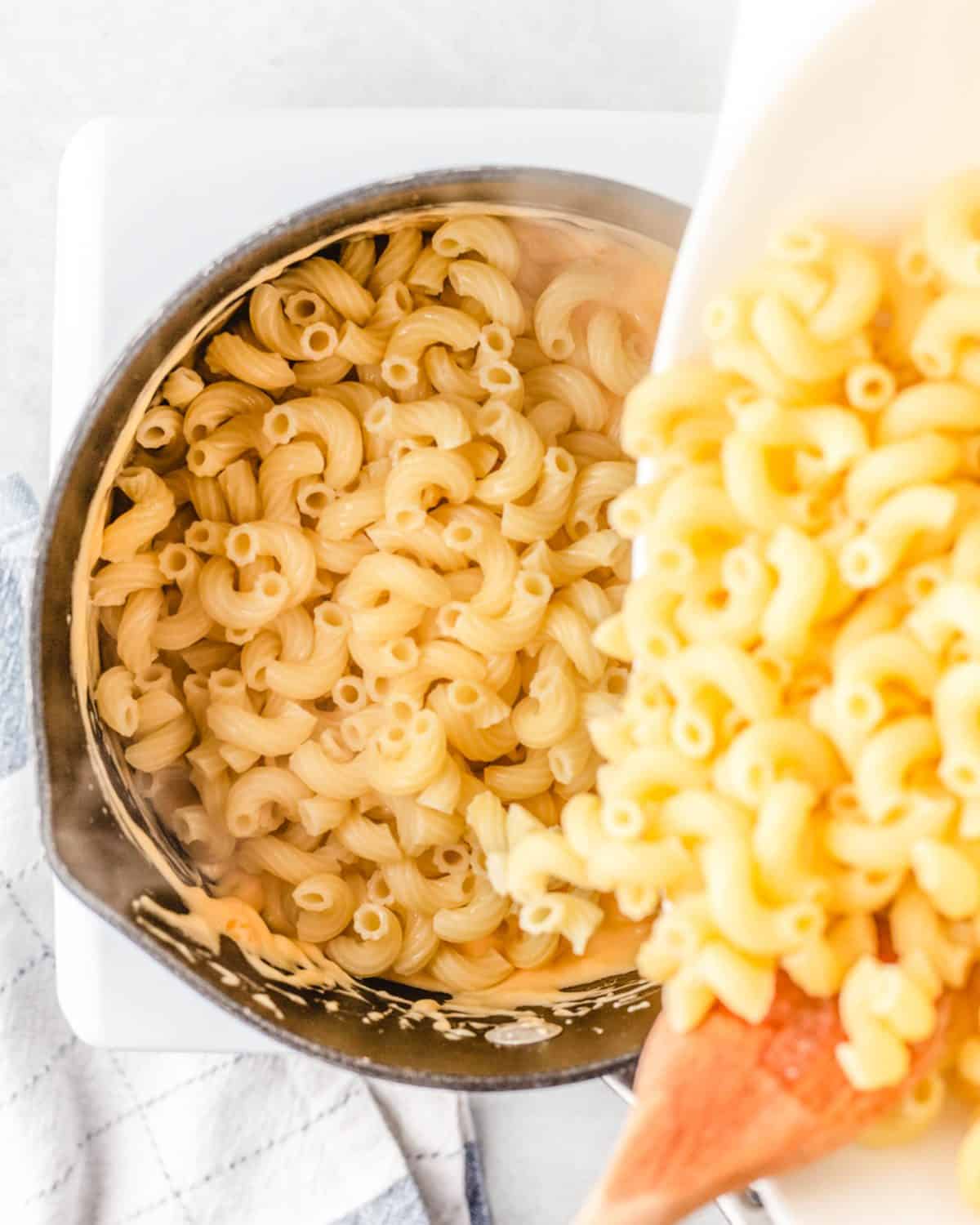 making macaroni and cheese cups - cooked elbow macaroni being poured into the saucepan with the cheese sauce