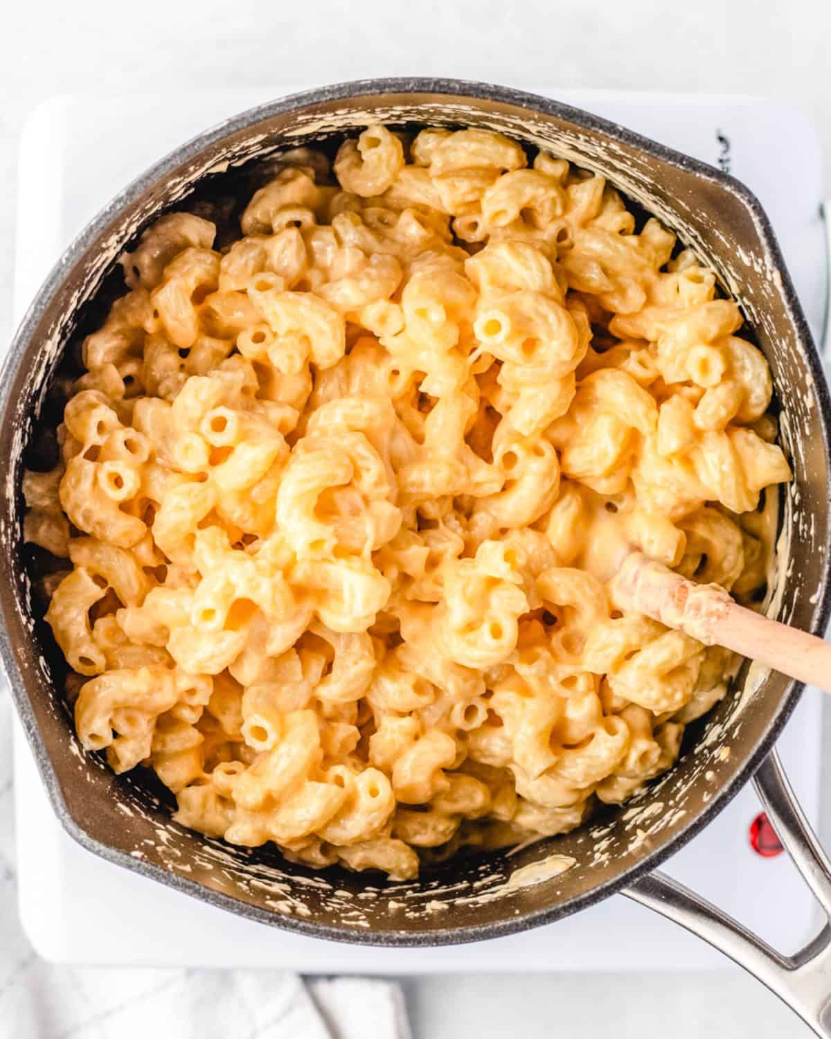 making macaroni and cheese cups - final mac and cheese mixture in a saucepan with a wooden spoon