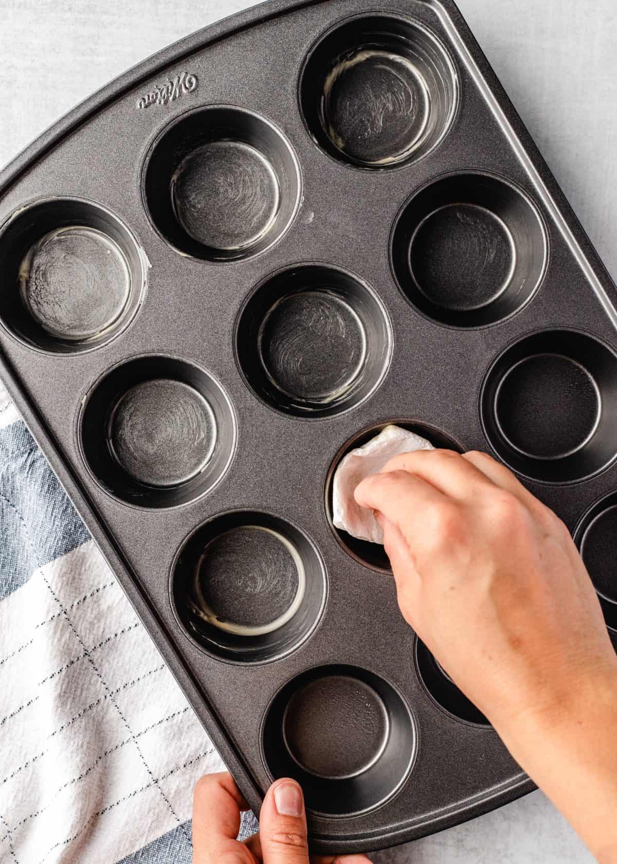 making macaroni and cheese cups - a hand buttering a 12 cup muffin pan.