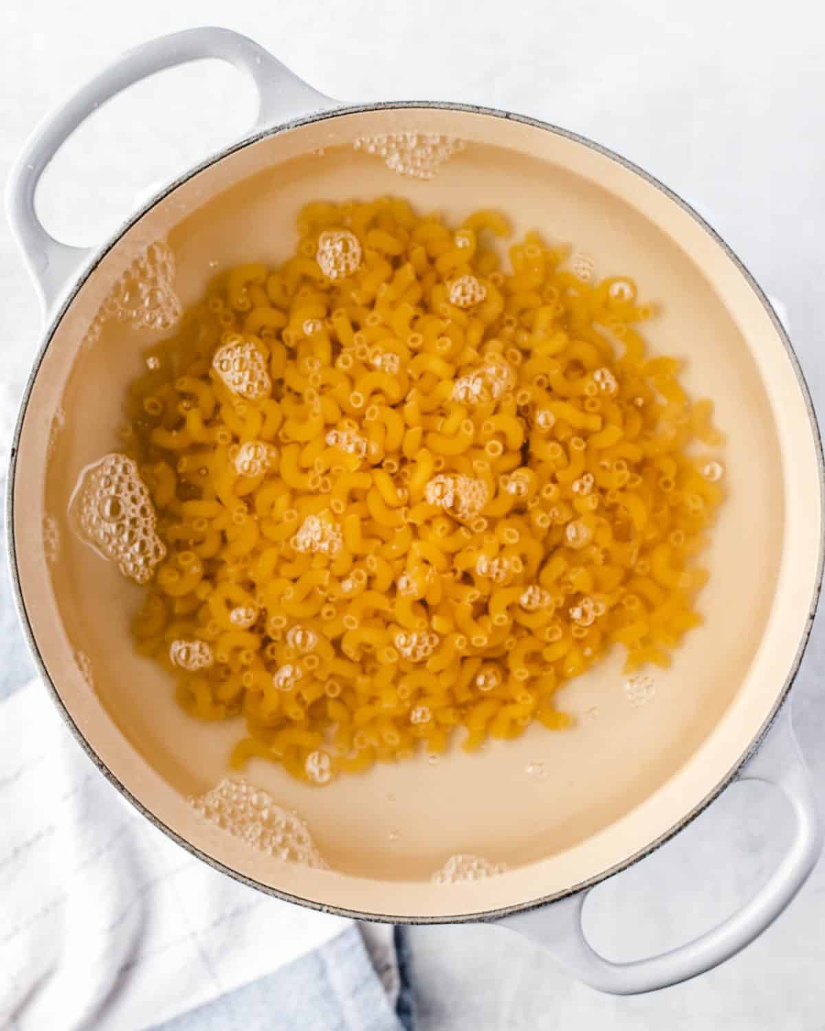 making mac and cheese cups - elbow macaroni noodles cooking in boiling water in a white pot