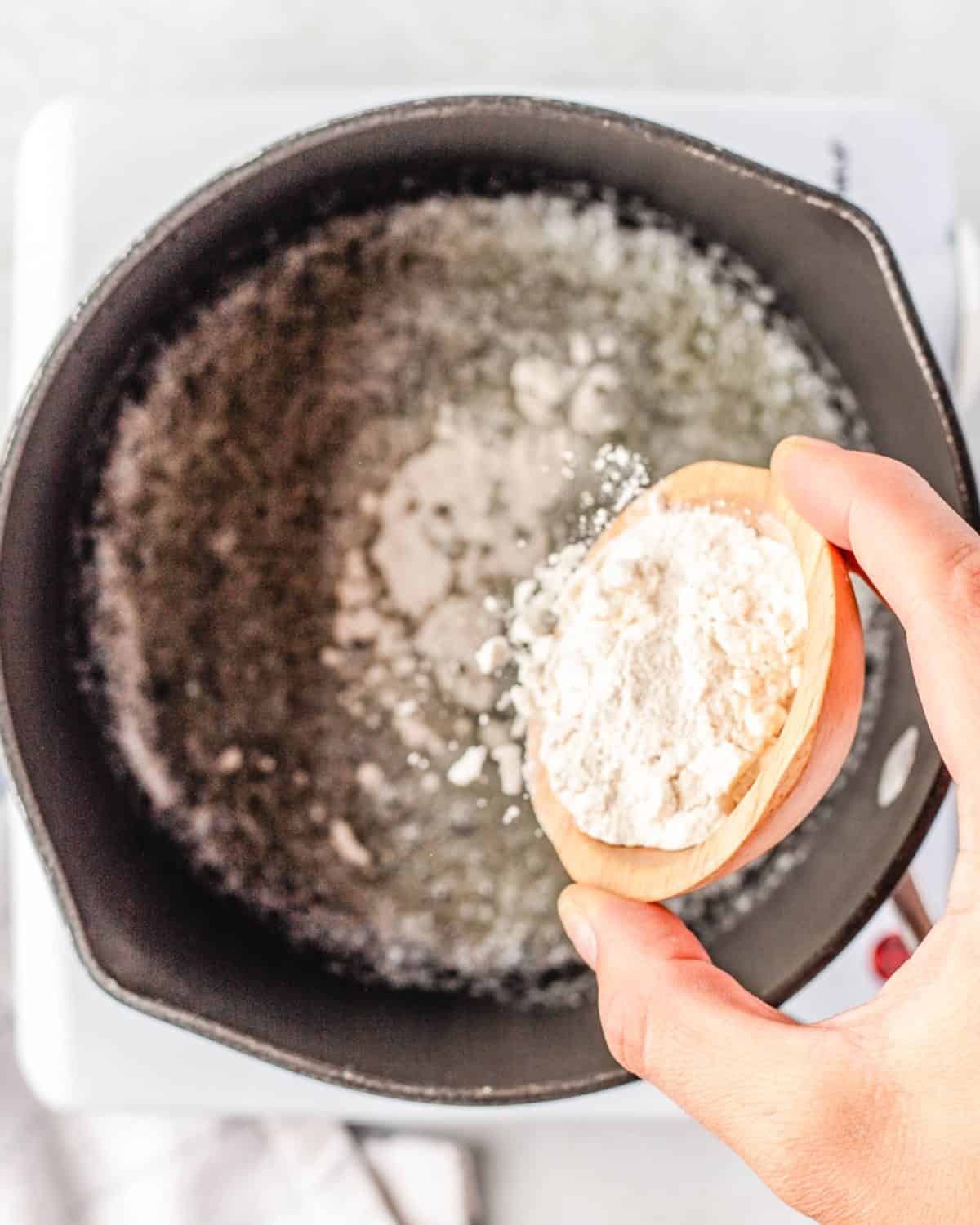 making mac and cheese cups - flour being poured into melted butter in a cast iron skillet to make a roux