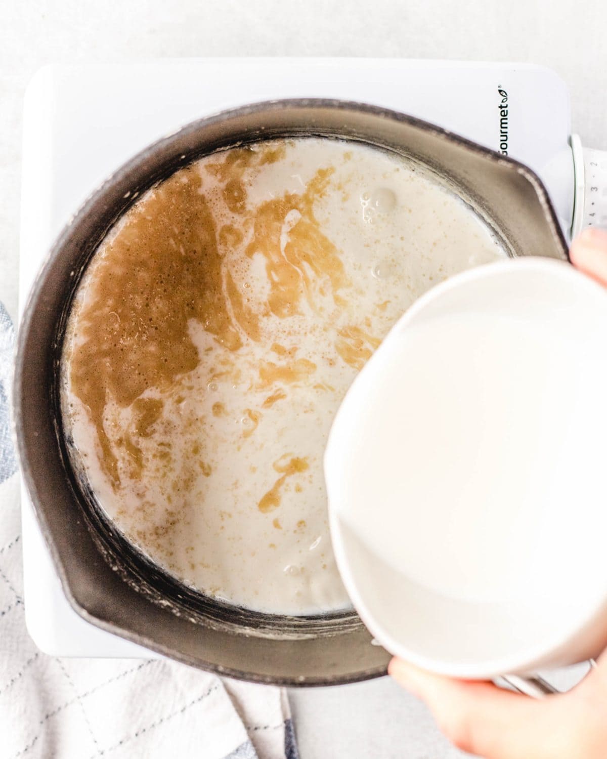 making macaroni and cheese cups - milk being poured into the roux in a black cast iron skillet.